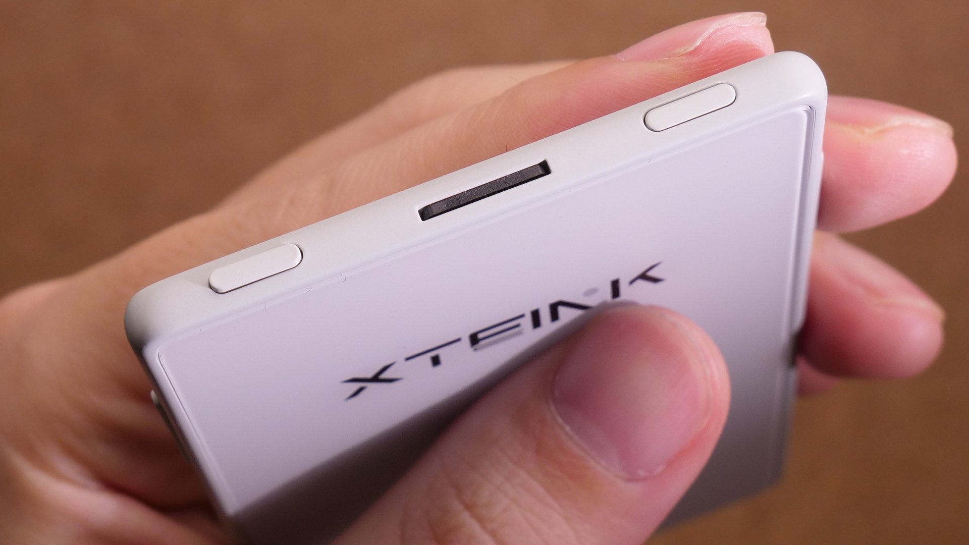Xteink X3を手に持ち、天面のmicroSDカードスロットと左右のボタンが見える角度から撮影した写真